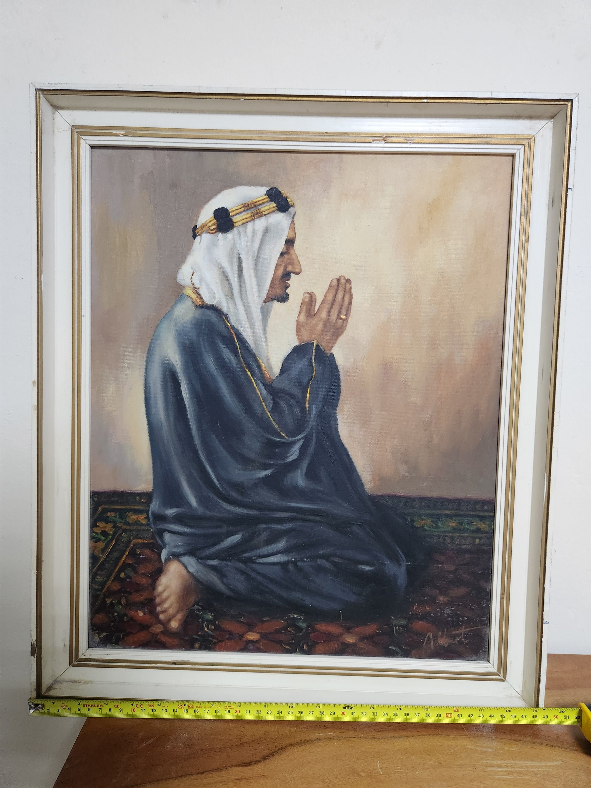 Orientalist oil painting of a man at prayer in ghutra and bisht, framed in white and gilt, shown with tape measure for width